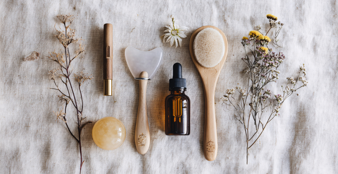 Skincare tools laying on a cream colored linen with dried herbs next to it
